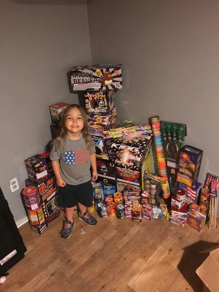 A little girl is standing in front of a pile of fireworks.