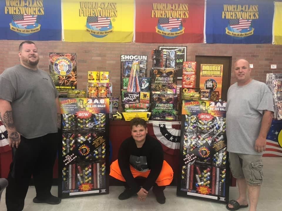 Three men are standing in front of a display of fireworks.