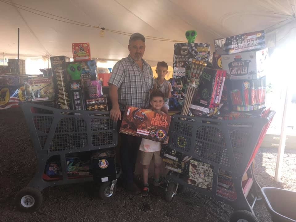 A man and two children are standing next to a shopping cart filled with toys.