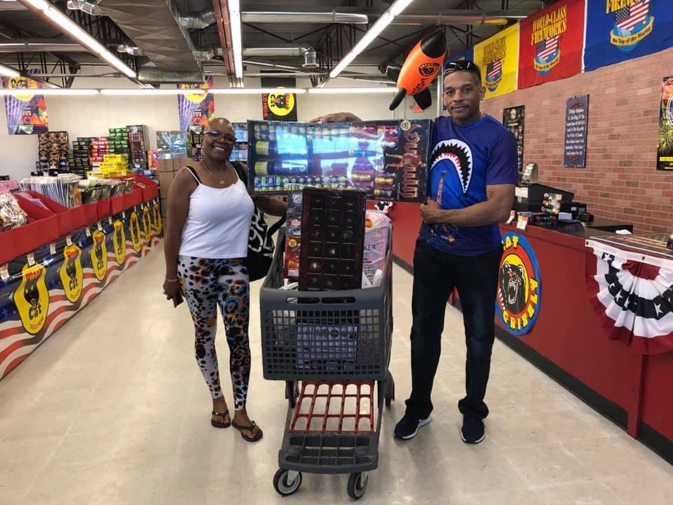 A man and a woman are standing next to a shopping cart in a store.