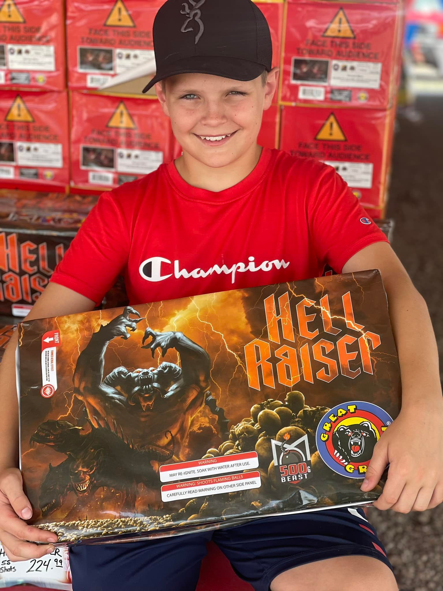 A young boy in a red shirt is holding a box of fireworks.