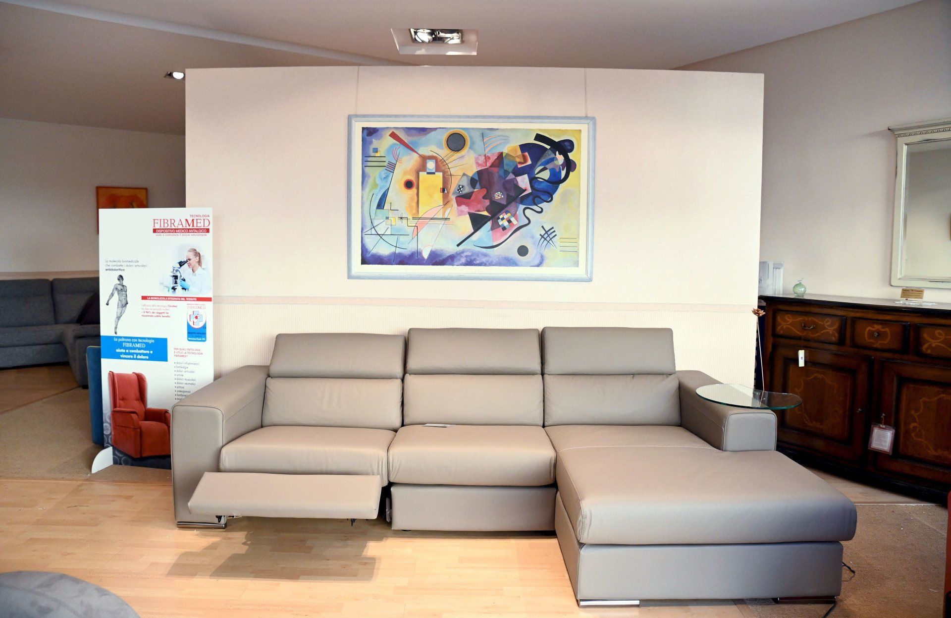 Atrio moderno con divano componibile beige, opere d'arte astratte alle pareti e un espositore per brochure accanto a un mobiletto in legno.