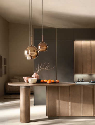 Cucina moderna con tavolo rotondo, lampade a sospensione e isola in legno dai toni neutri e caldi.