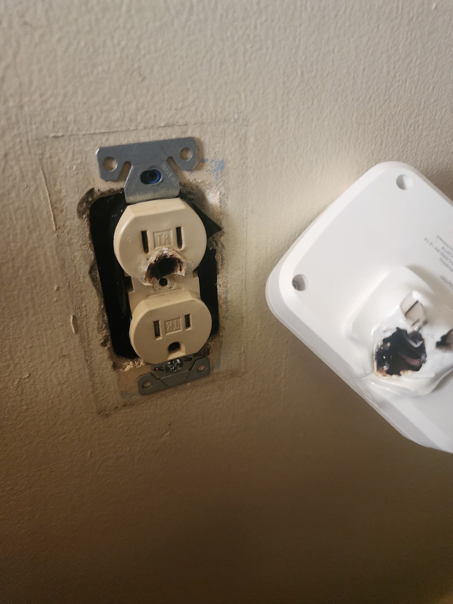 Close-up of a worn wall outlet with a white plug cover hanging beside it.