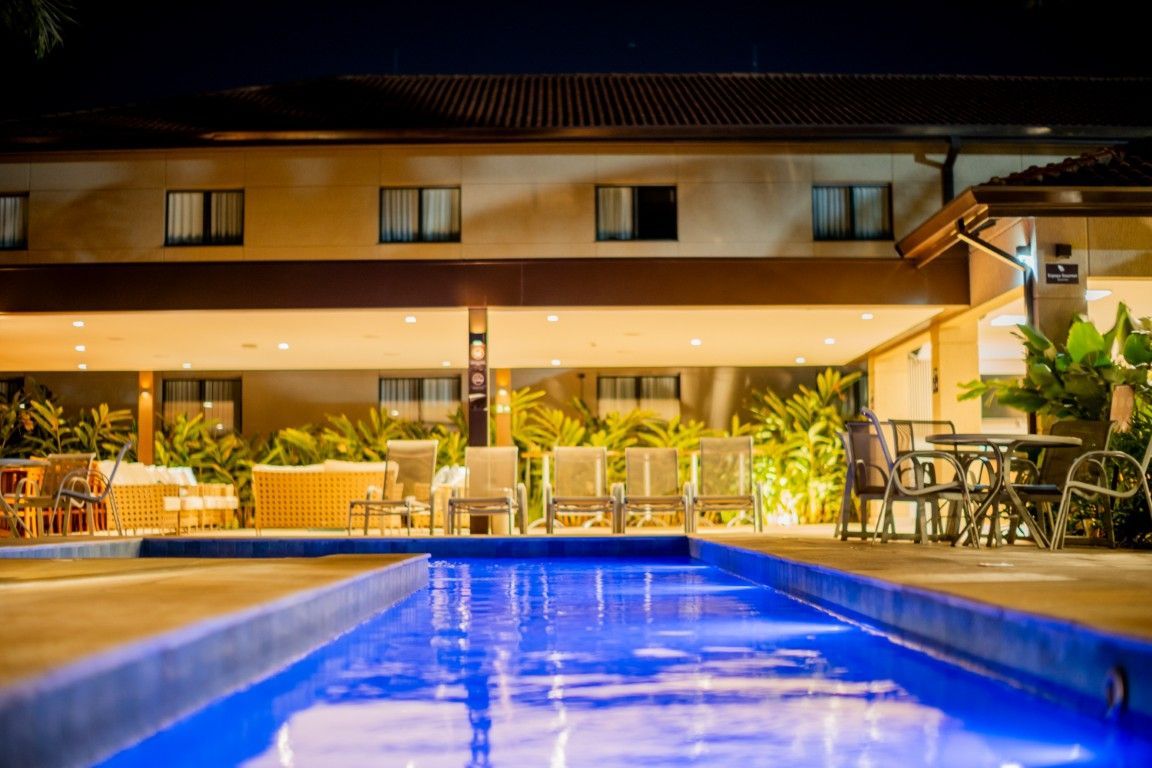 Uma grande piscina é iluminada à noite em frente a um hotel.