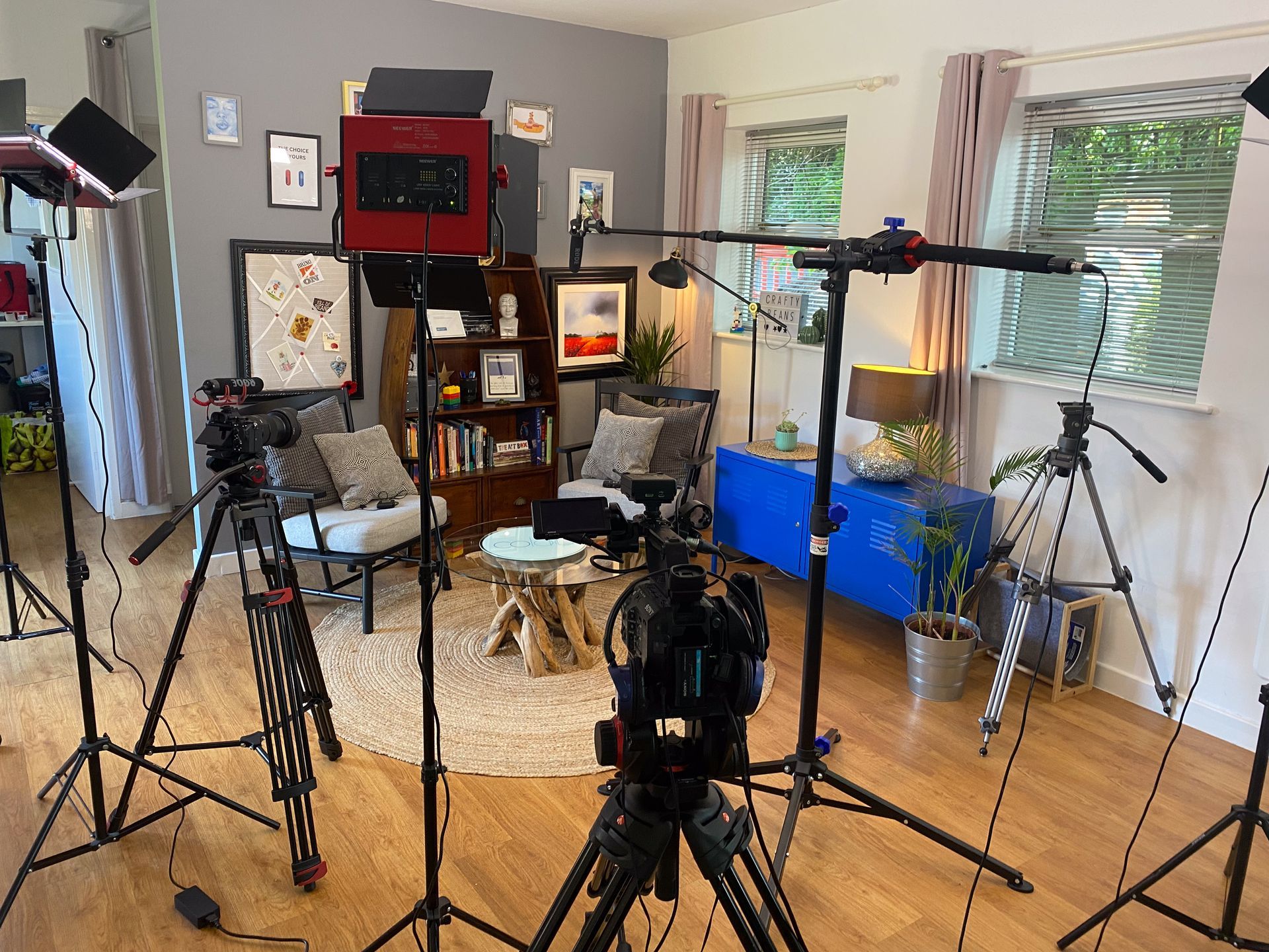 A living room set up as a professional video studio, featuring chairs, lights on stands, and multiple cameras on tripods.