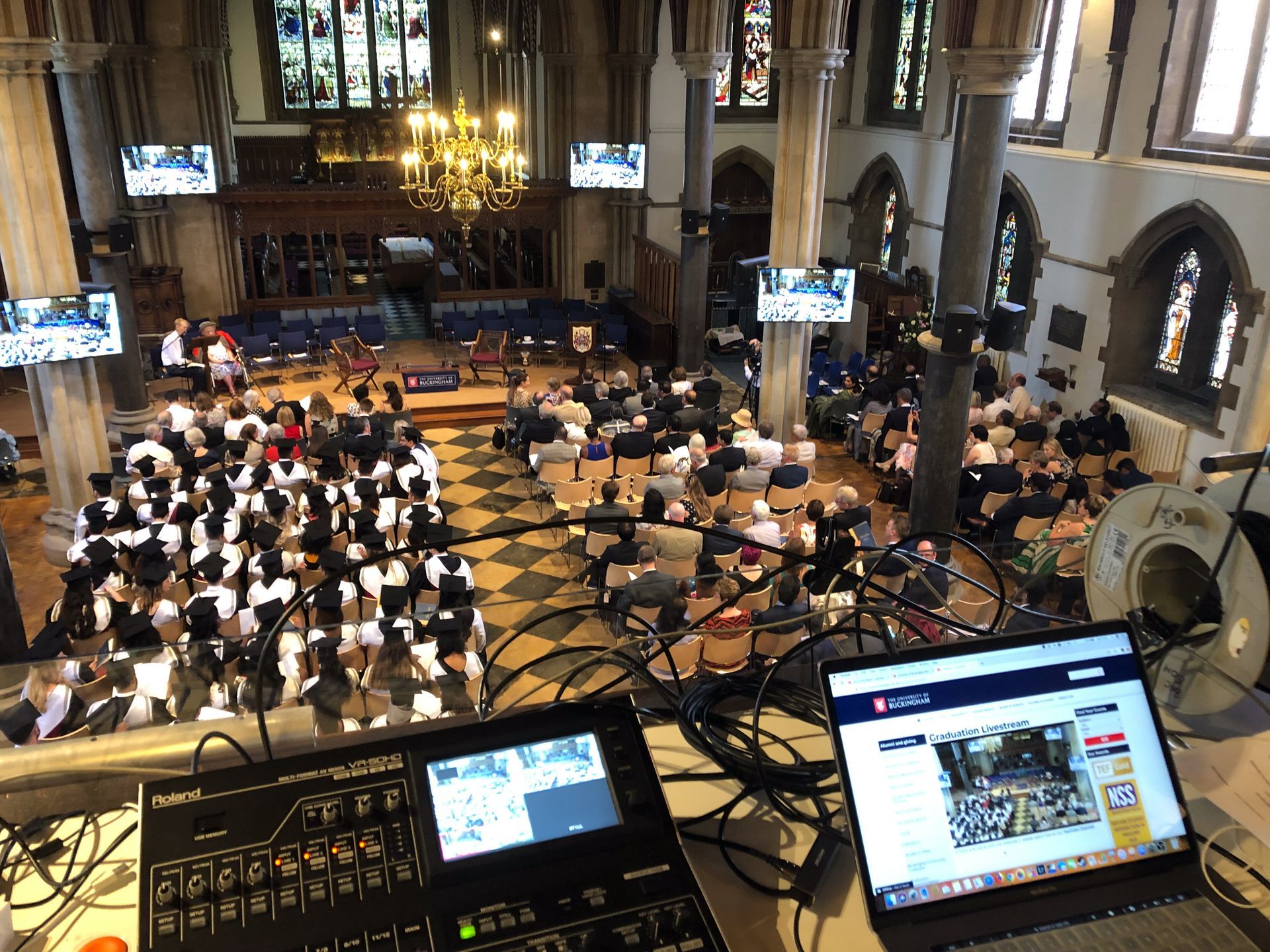 A view from an audio-visual control station, overlooking an indoor event audience seated in a historic church hall.