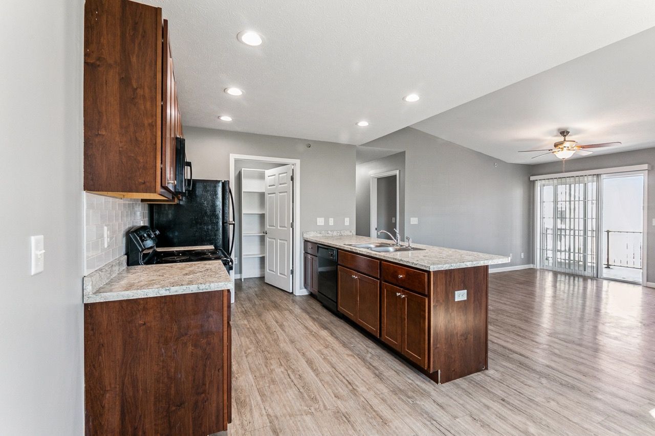 Modern kitchen with brown cabinets, light countertops, and gray walls, connected to a living area with sliding glass doors.