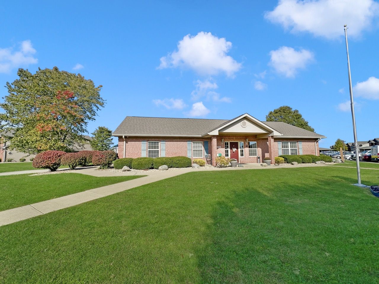 Brick building with a green lawn and a sidewalk under a blue sky with fluffy white clouds.