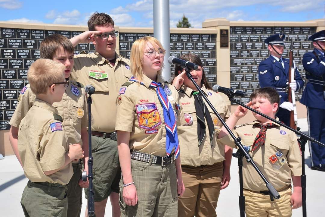 A group of boy scouts are singing into microphones.