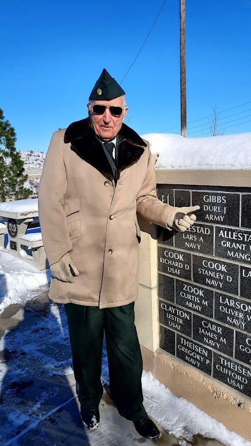 A man in a military uniform is standing next to a wall in the snow.