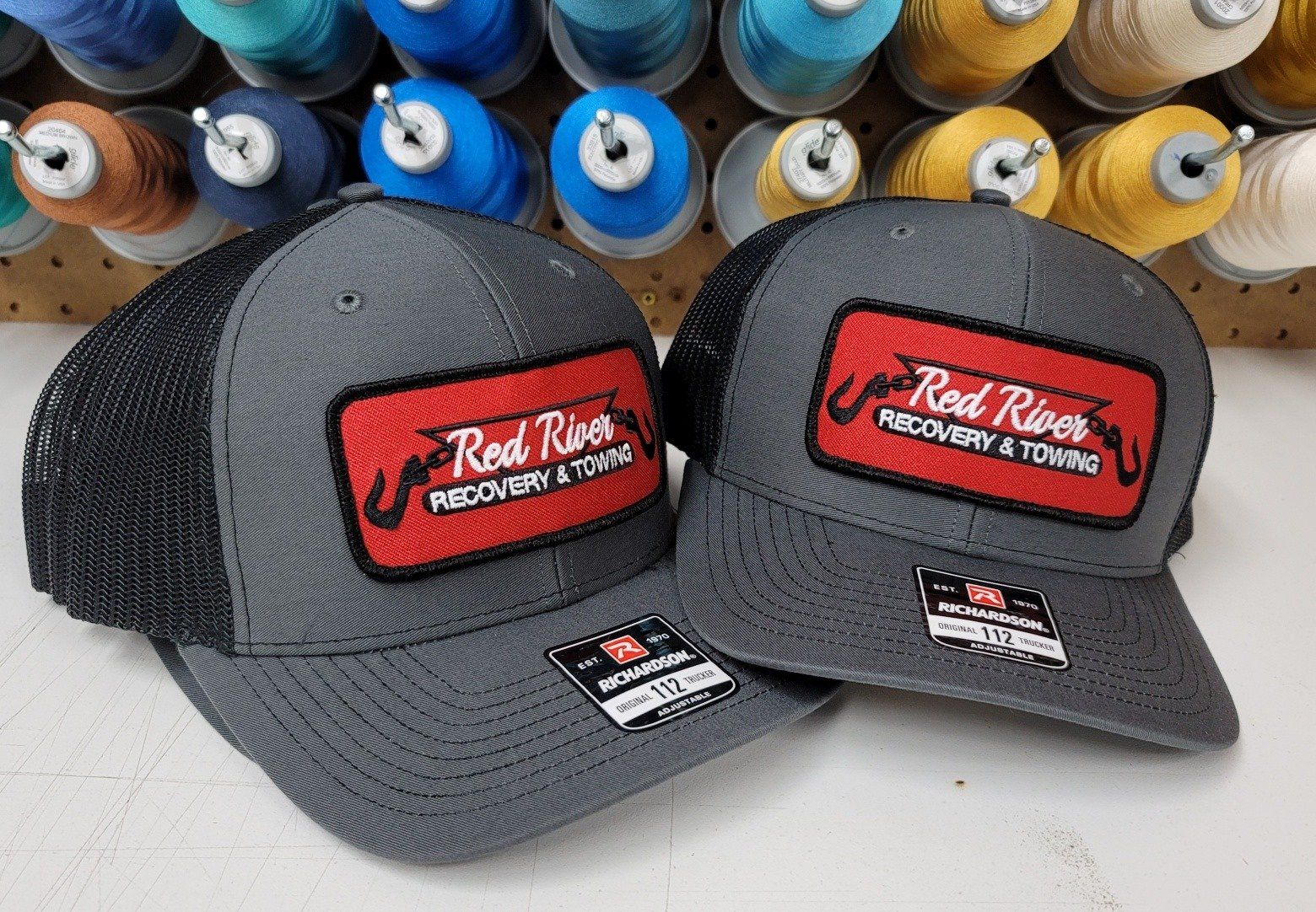 Two gray trucker hats with black mesh backs, each with a red patch reading