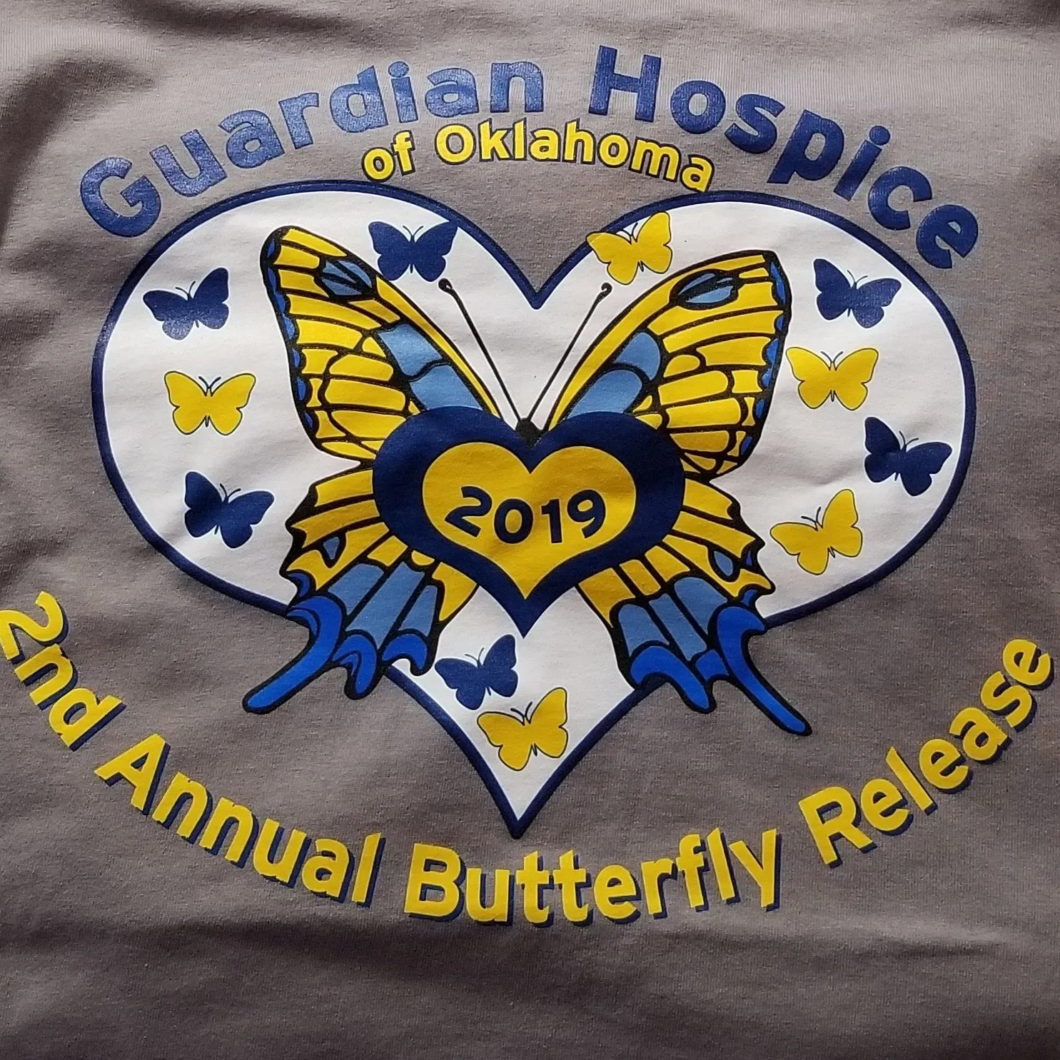 Gray shirt with a heart-shaped design: Guardian Hospice of Oklahoma, 2nd Annual Butterfly Release. Butterfly image in blue, yellow, and white.