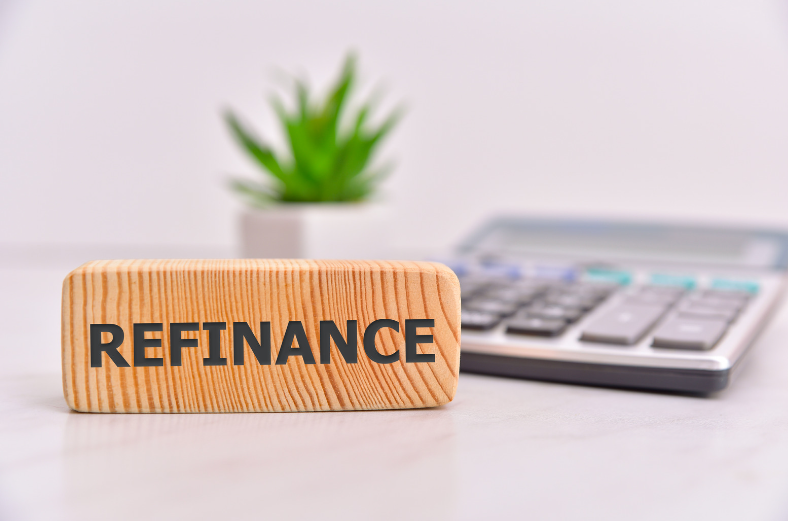 A wooden block with the word refinance written on it is sitting on a table next to a calculator.