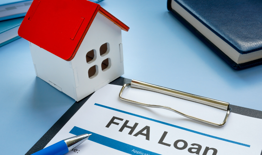 A small model house is sitting on top of a clipboard with a pen.