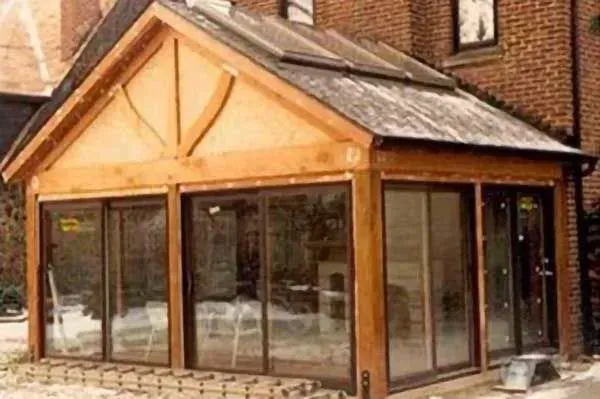 Glass-fronted wooden porch with a pitched roof attached to a brick building