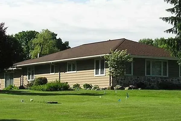 Single-story tan house with brown roof and green lawn in a suburban setting
