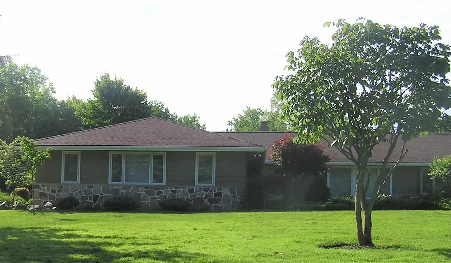 Single-story house with a red roof and large green lawn under trees in bright sunlight