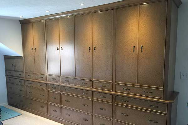 Wall of built-in wooden cabinets with drawers and brass handles in a room