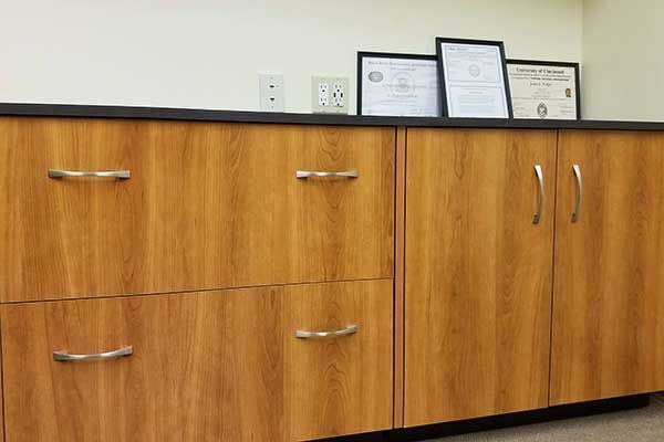 Wooden office cabinet with silver handles and framed certificates on top against a light wall