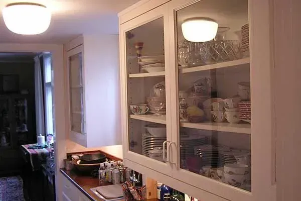 Kitchen with white cabinets, countertop appliances, and warm overhead lights leading into a dining area