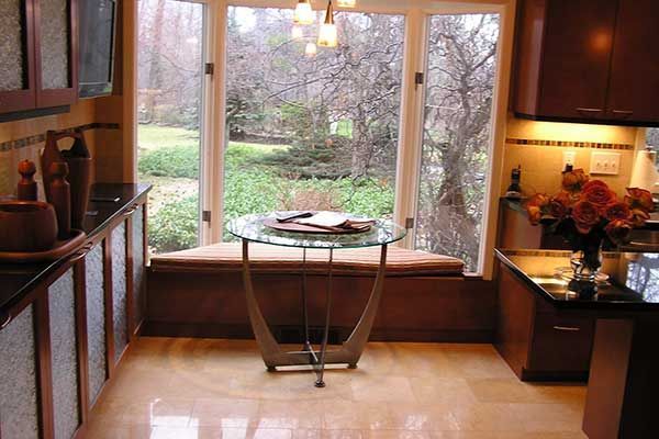 Cozy kitchen nook with bay window, small glass table, and cabinets, overlooking a garden
