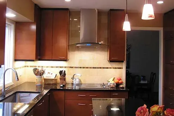 Modern kitchen with dark wood cabinets, stainless range hood, black countertops, and hanging pendant lights