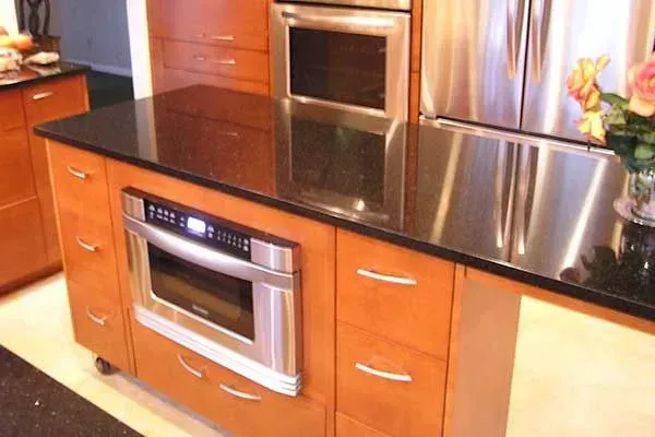 Modern kitchen with wooden cabinets, black countertop, stainless steel oven and microwave, and stainless refrigerator