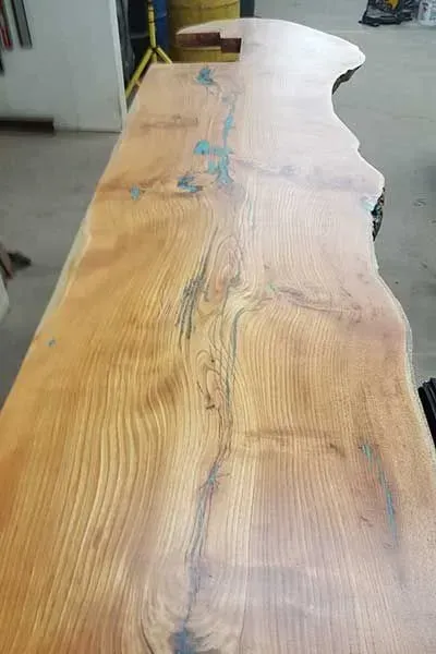 Large wooden tabletop with natural grain and a wavy live-edge shape in a workshop.