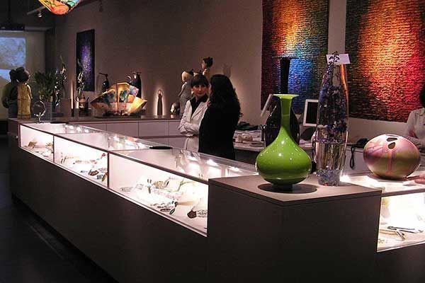 Museum exhibit of glass vases and pottery in a dimly lit gallery, with a visitor viewing the display.