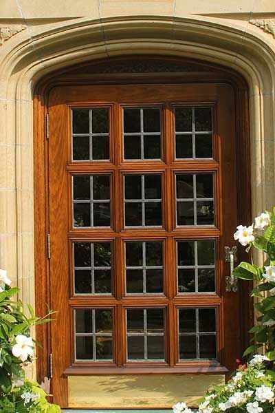 Wooden-framed window with multiple panes set in a stone wall, surrounded by greenery and white flowers