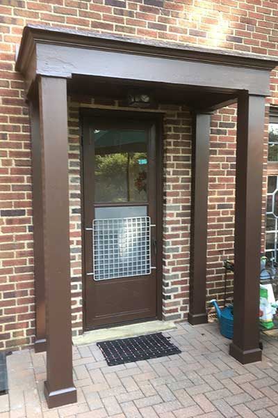 Brick entryway with a brown door, narrow columns, and a small mat at the doorstep