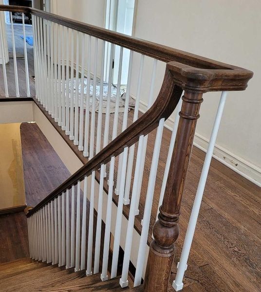 Wooden stair railing with white balusters and a dark handrail in a hallway
