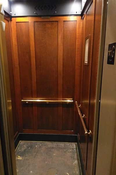 Wood-paneled elevator interior with brass handrails and a worn floor.