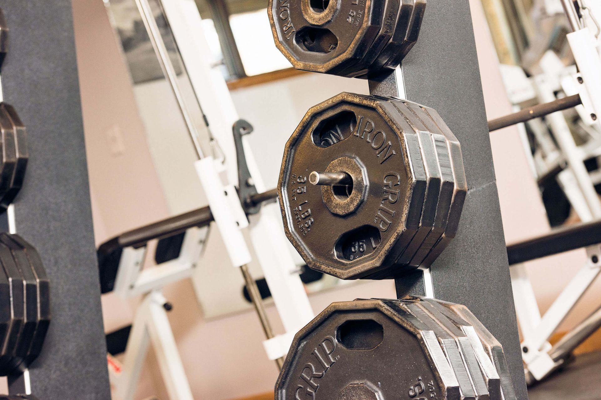 Weight plates stacked on a rack in a gym, with other workout equipment in the background.