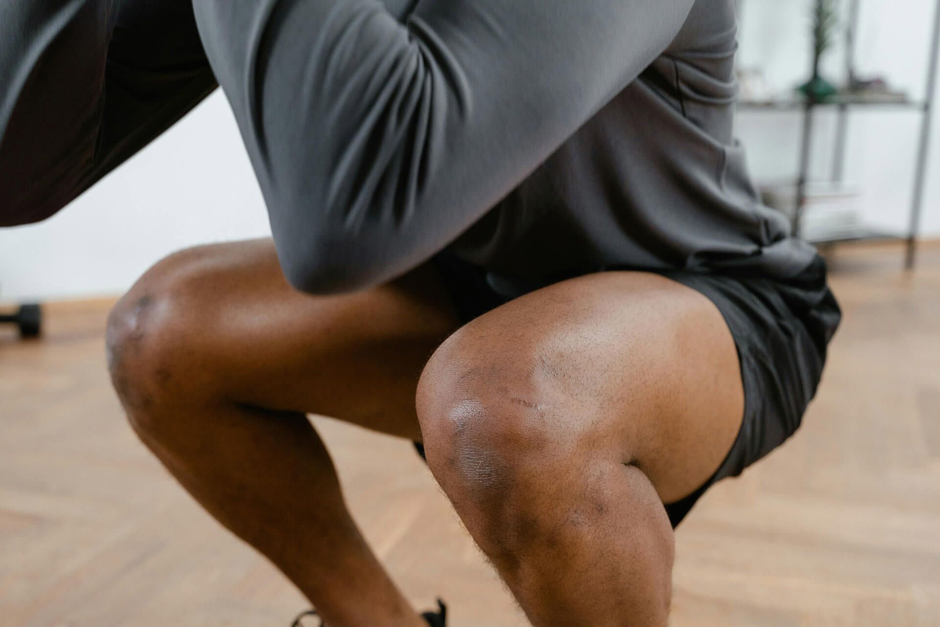A person in a gray long-sleeved shirt and black shorts performing a deep squat in a gym setting.