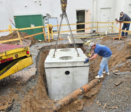 A worker in blue hard hat tightens pipes with a wrench, wearing gloves and safety glasses.