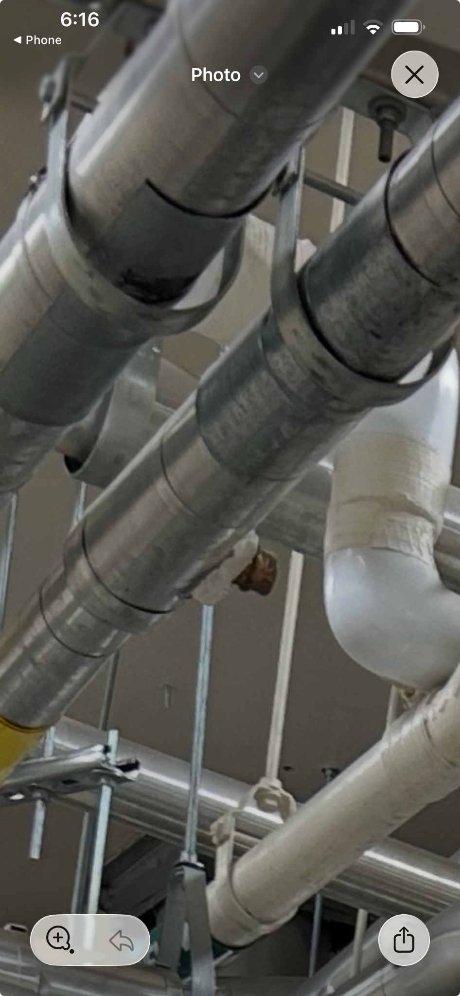 A worker in a hard hat and safety glasses inspects pipes on a ceiling.