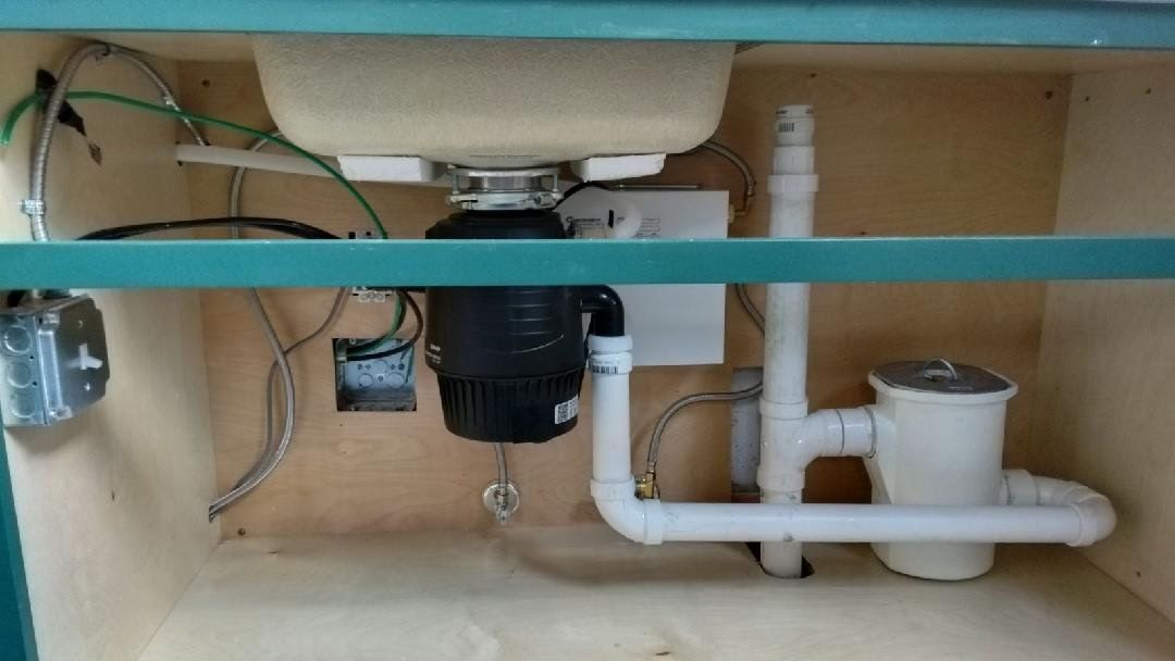 Man kneeling in bathroom, working on plumbing under sink.
