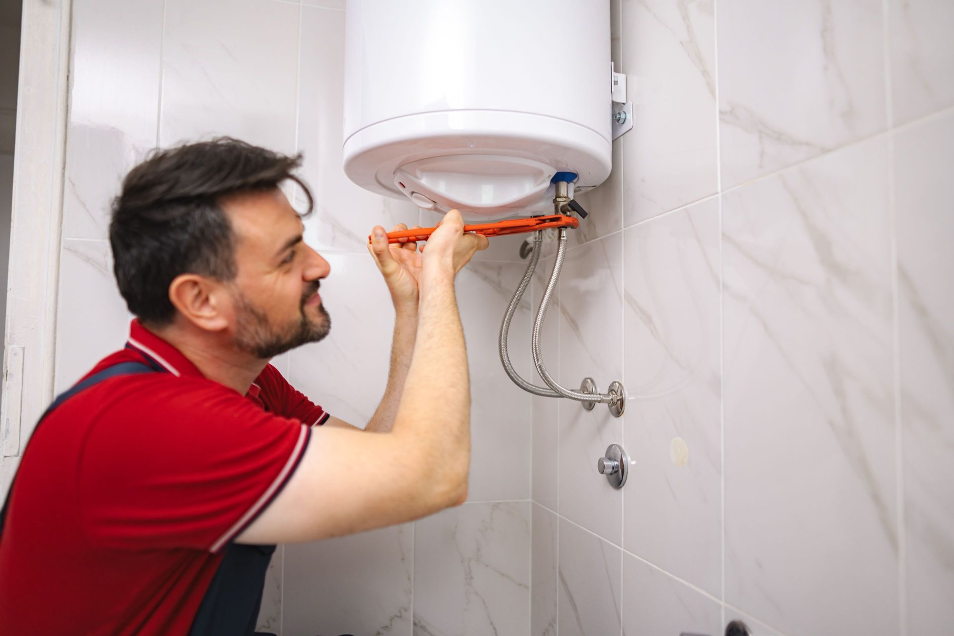 Man in red shirt, fixing a water heater with a wrench in a bathroom. Man in red shirt, fixing a water heater with a wrench in a bathroom.