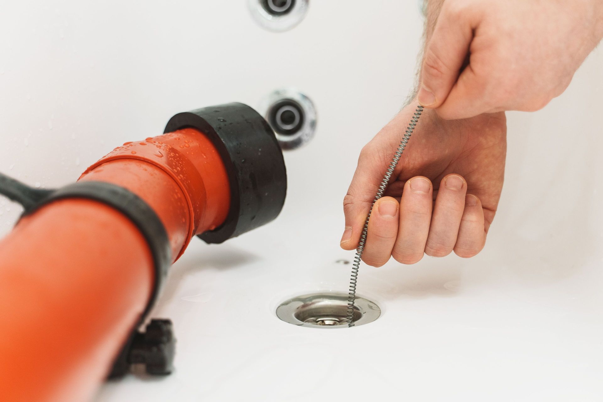 Person pulling the chain on a bathtub drain, with a plunger visible nearby. Person pulling the chain on a bathtub drain, with a plunger visible nearby.