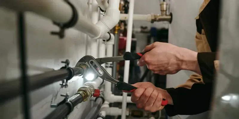 A person using pliers on a pipe in a utility room. A person using pliers on a pipe in a utility room.