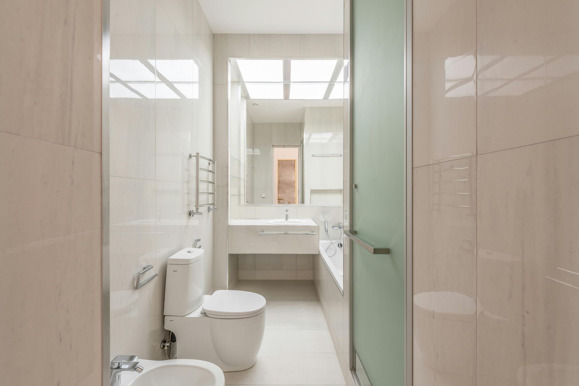 Modern, white bathroom with toilet, bidet, sink, and glass shower door.