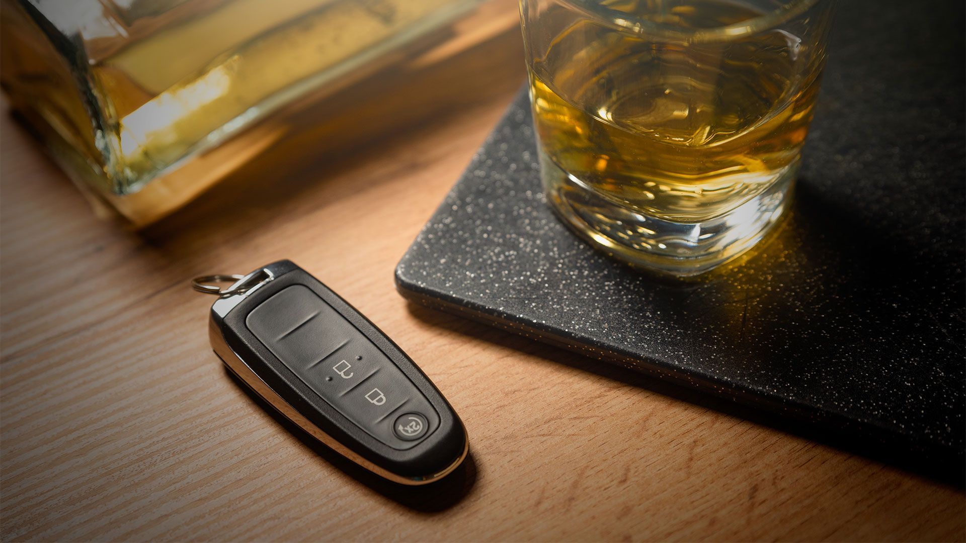 A car key and a glass of whiskey are on a wooden table.