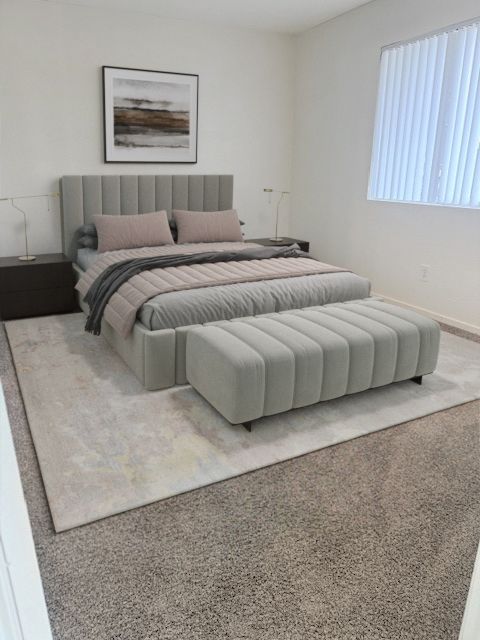 A neutral-toned bedroom features a tufted gray bed with matching bench, two dark nightstands, and abstract wall art.