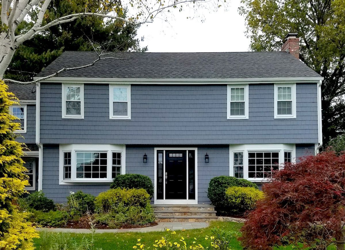Two-story blue house with white trim, bay windows, black door, and landscaping.