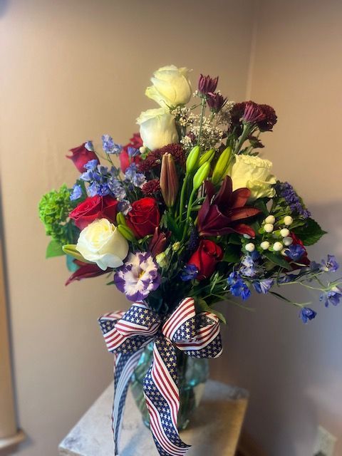 A vase filled with red white and blue flowers with an american flag bow