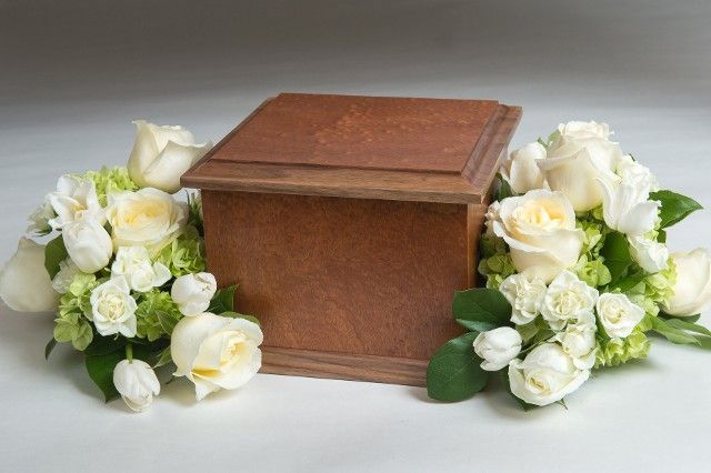 A wooden box is surrounded by white roses and greenery.
