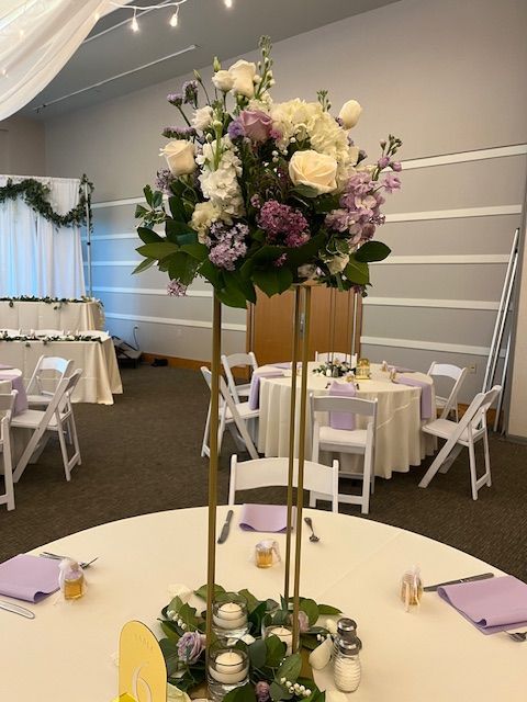 A tall vase filled with purple and white flowers sits on a table.