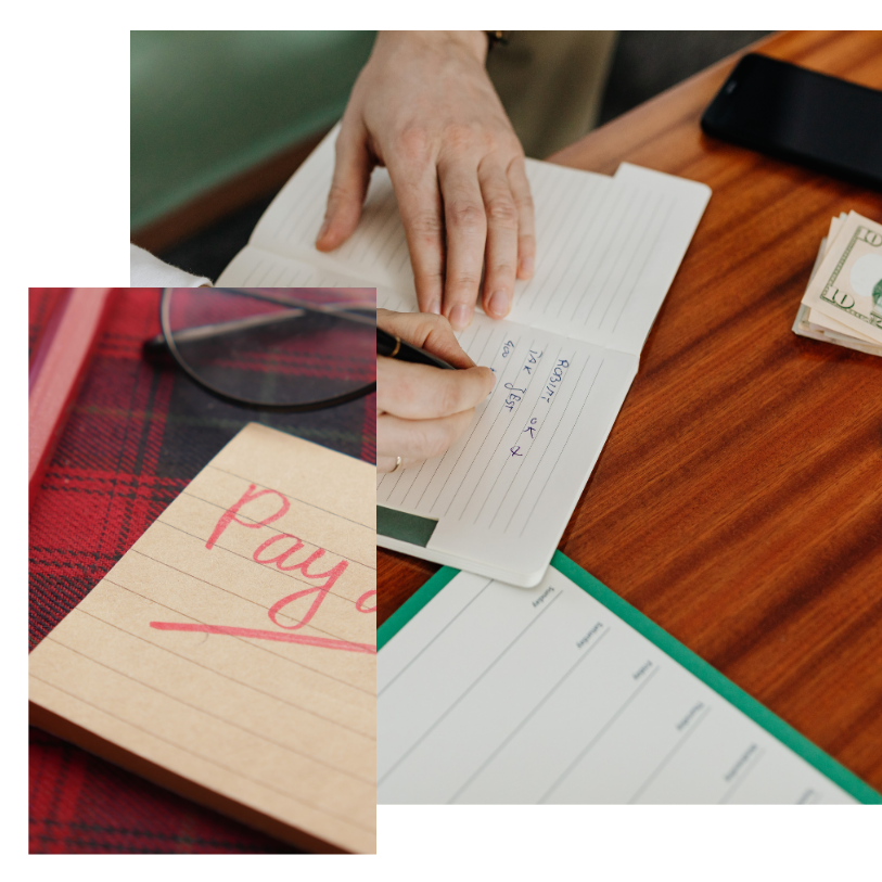 Hand writing a check on a desk beside a red notebook and papers